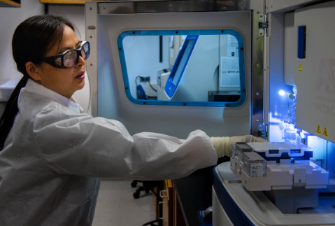 Woman in lab wearing white coat using medical equipment